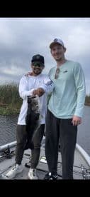Two anglers proudly displaying a large Largemouth Bass while fishing on a freshwater lake.