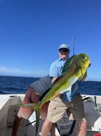 An angler proudly displaying a large Mahi Mahi aboard a fishing boat, showcasing a successful day on the water.
