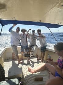 Group of anglers enjoying a fishing trip on a boat, showcasing their excitement while reeling in fish in sunny waters.