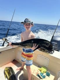 A young angler proudly displaying a large Mahi Mahi on a fishing boat, showcasing a successful day on the water.