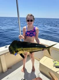 A young angler proudly displaying a vibrant Mahi Mahi while fishing on a sunny day at sea.