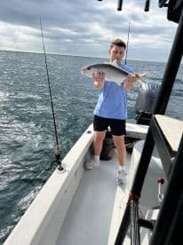 A young angler proudly displaying a caught fish while aboard a fishing boat in open waters.
