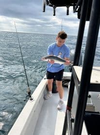 A young angler is reeling in a fish while on a boat, showcasing the excitement of fishing in open waters.