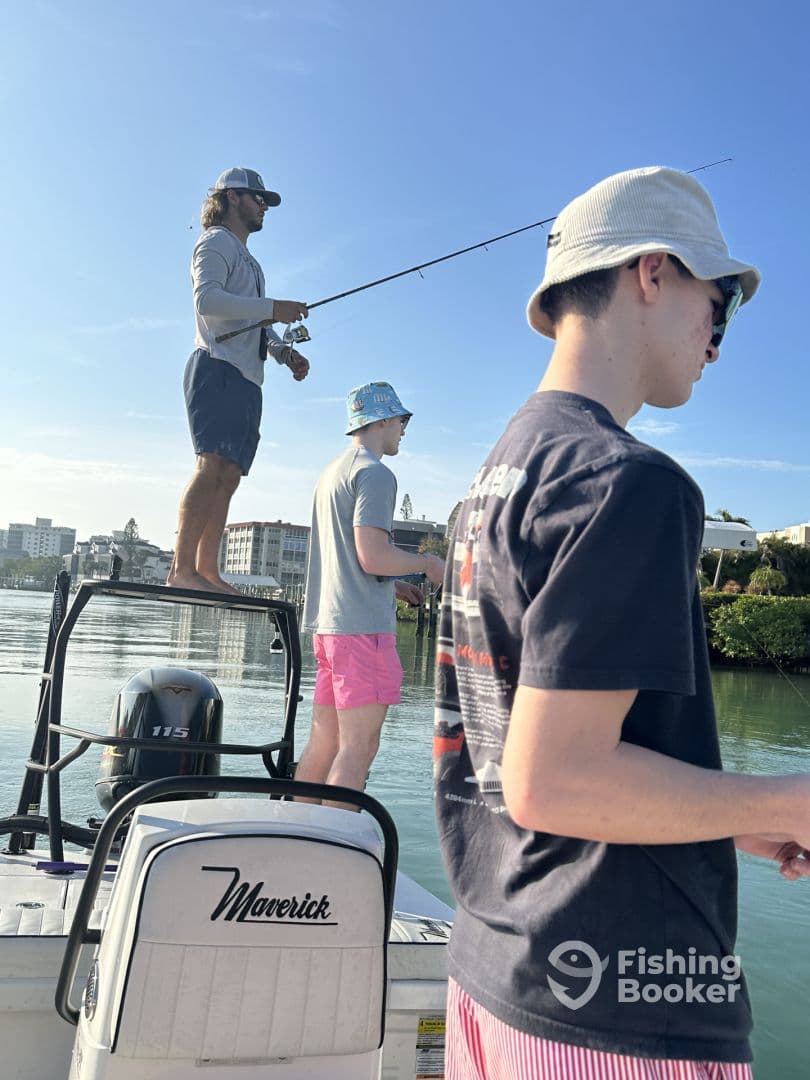 Group of young anglers fishing from a Maverick boat in calm waters, showcasing an active fishing experience under clear skies.