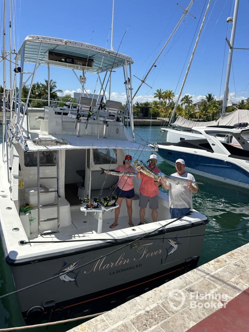 Three anglers proudly displaying a large fish aboard the Marlin Fever in La Romana, showcasing a successful fishing trip.