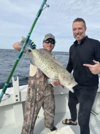 Two anglers proudly displaying a large Grouper caught during a deep-sea fishing trip.