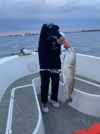 Young angler holding a large fish on a boat during a fishing trip, showcasing a successful catch.