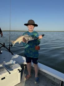 A young angler proudly displaying a Redfish while fishing on a sunny day, showcasing the excitement of youth fishing adventures.