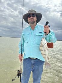 An angler proudly displaying a large fish while fishing in a calm water environment, showcasing a successful day on the water.
