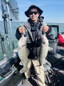 Young angler proudly displaying two Walleye caught during a fishing trip on a boat.