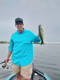 An angler proudly displaying a large Largemouth Bass while fishing from a boat on a calm lake.