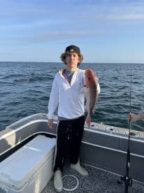 Young angler proudly displaying a Red Snapper while fishing offshore, showcasing a successful day on the water.