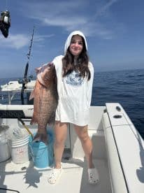A young angler proudly displaying a large Snapper while fishing on a boat in open waters.