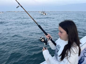 A young angler focused on reeling in a catch while fishing from a boat in open waters.