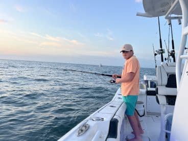 A young angler casting off from a modern fishing boat during a serene sunset on the open water.