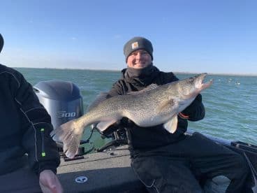 Angler proudly displaying a large Walleye while fishing on a boat in a scenic waterway.