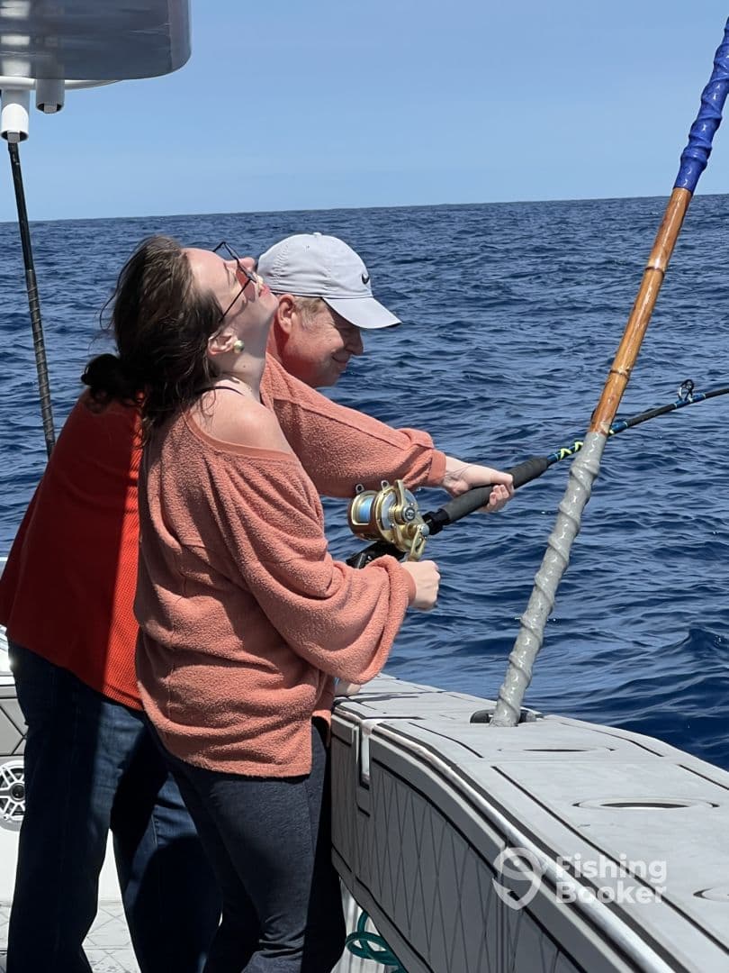 Two anglers engaged in reeling in a catch while enjoying a sunny day on the open ocean.