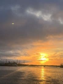 A scenic sunset over the water, with silhouettes of boats and masts in the background, creating a tranquil fishing environment.