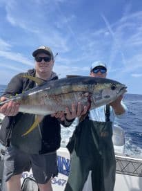 Two anglers proudly displaying a large Yellowfin Tuna while out on the open ocean, showcasing a successful fishing trip.