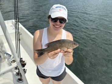 A young woman proudly displaying her catch, a Snook, while fishing on a boat in calm waters.