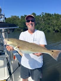 An angler proudly displaying a large Redfish while fishing in a mangrove area, showcasing a successful day on the water.