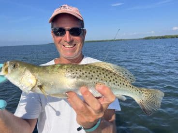 An angler proudly displaying a Speckled Trout while fishing in a scenic coastal environment.
