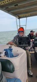 A cheerful angler at the helm of a fishing boat, equipped with a fish finder, enjoying a day on the water.