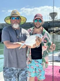 Two anglers proudly displaying a caught fish while enjoying a sunny day on the water, showcasing a vibrant fishing environment.