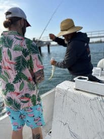 A young angler is actively reeling in a fish while being guided by an experienced fisherman on a boat, showcasing a vibrant fishing environment.