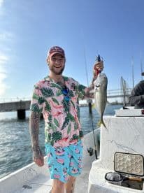 A young man proudly displaying a caught fish while enjoying a day on the water, dressed in vibrant tropical attire.