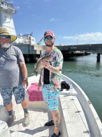 Two anglers on a boat proudly displaying a caught fish, with a vibrant fishing environment in the background.
