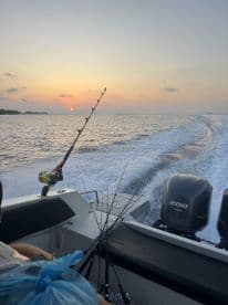 A scenic view from inside a boat at sunset, showcasing fishing rods ready for action as the boat cruises through calm waters.