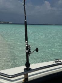 A fishing rod positioned on the edge of a boat with clear turquoise waters in the background, suggesting a serene fishing environment.