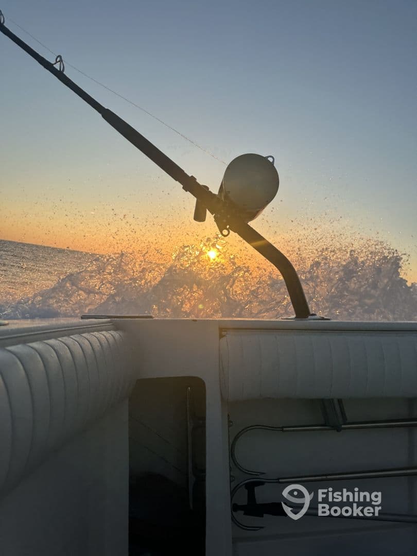 A scenic view from inside a boat, capturing the fishing rod and the sun setting over the ocean, creating a tranquil atmosphere.
