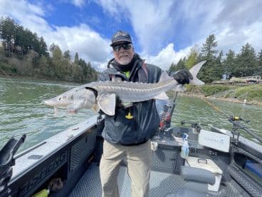 An angler proudly displaying a large Sturgeon while fishing from a boat in a scenic river setting.