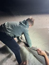 A young angler assisting in the catch of a large fish on the beach during a nighttime fishing adventure.