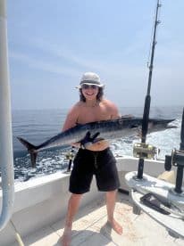 Young angler proudly holding a large Wahoo while fishing offshore, showcasing a successful day on the water.