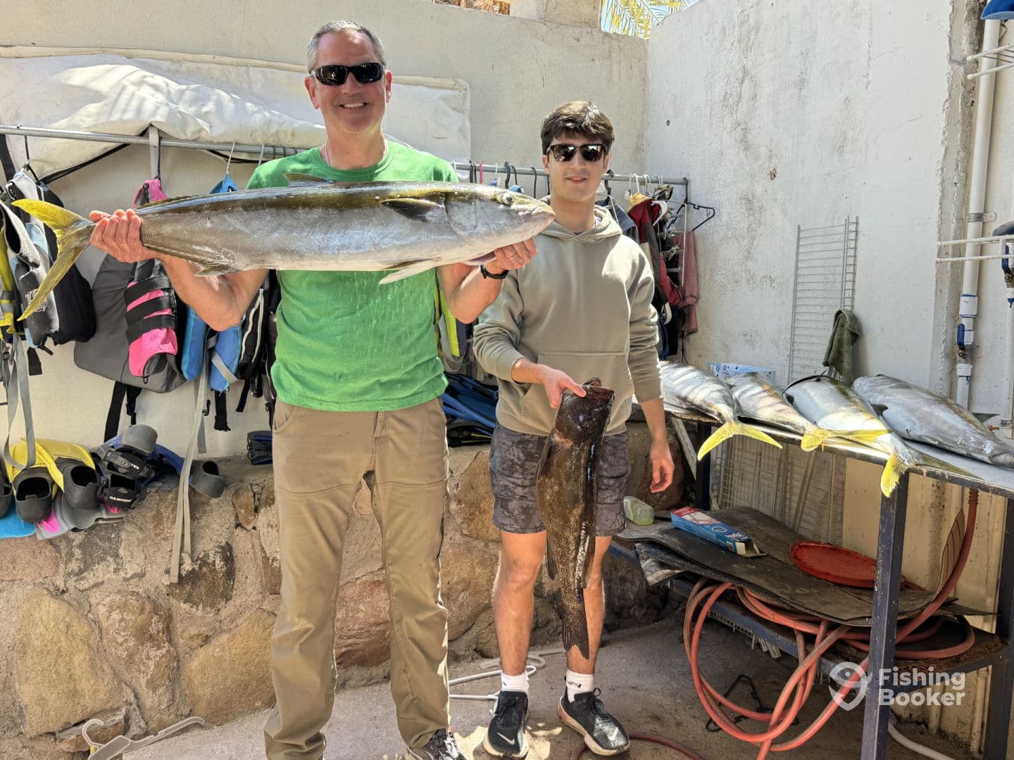 Two anglers proudly displaying their catch, including a large Yellowtail and a Grouper, at a fishing facility.