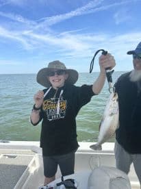 A young angler proudly displaying a large Speckled Trout while fishing on a boat, showcasing a sunny day on the water.