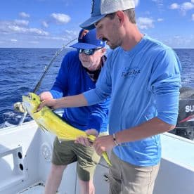 Two anglers on a boat proudly displaying a vibrant Mahi Mahi during a deep-sea fishing trip.