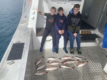 Three young anglers sitting on the boat with a catch of Snapper displayed on the deck after a successful fishing trip.