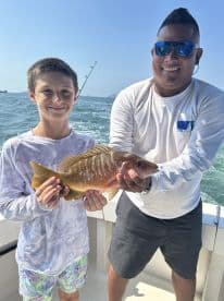A young angler and a guide proudly displaying a colorful Snapper caught during a fishing trip.