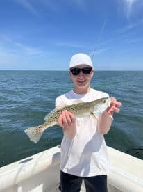 A young angler proudly displaying a Speckled Trout while fishing on a sunny day.