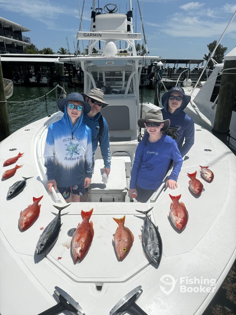 A family group poses on a fishing charter boat, showcasing a variety of freshly caught fish, including Snapper and Mackerel, arranged neatly on the deck.