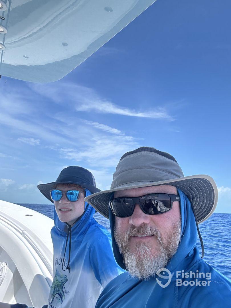 Two anglers enjoying a sunny day on a boat, showcasing a relaxed atmosphere with clear blue skies and ocean views.