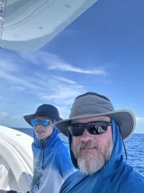 Two anglers enjoying a sunny day on a boat, showcasing a relaxed atmosphere with clear blue skies and ocean views.