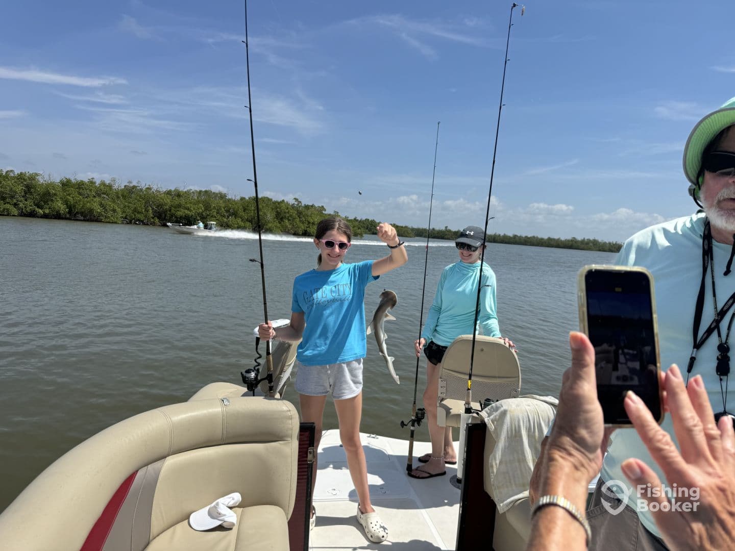 A young angler proudly displaying a caught fish while fishing on a boat in a scenic waterway, surrounded by family.