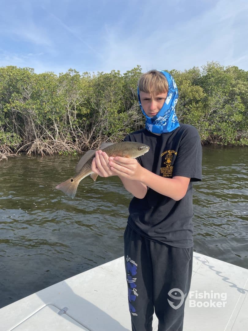 A young angler proudly displaying a Redfish while fishing in a mangrove area, showcasing the excitement of a successful catch.