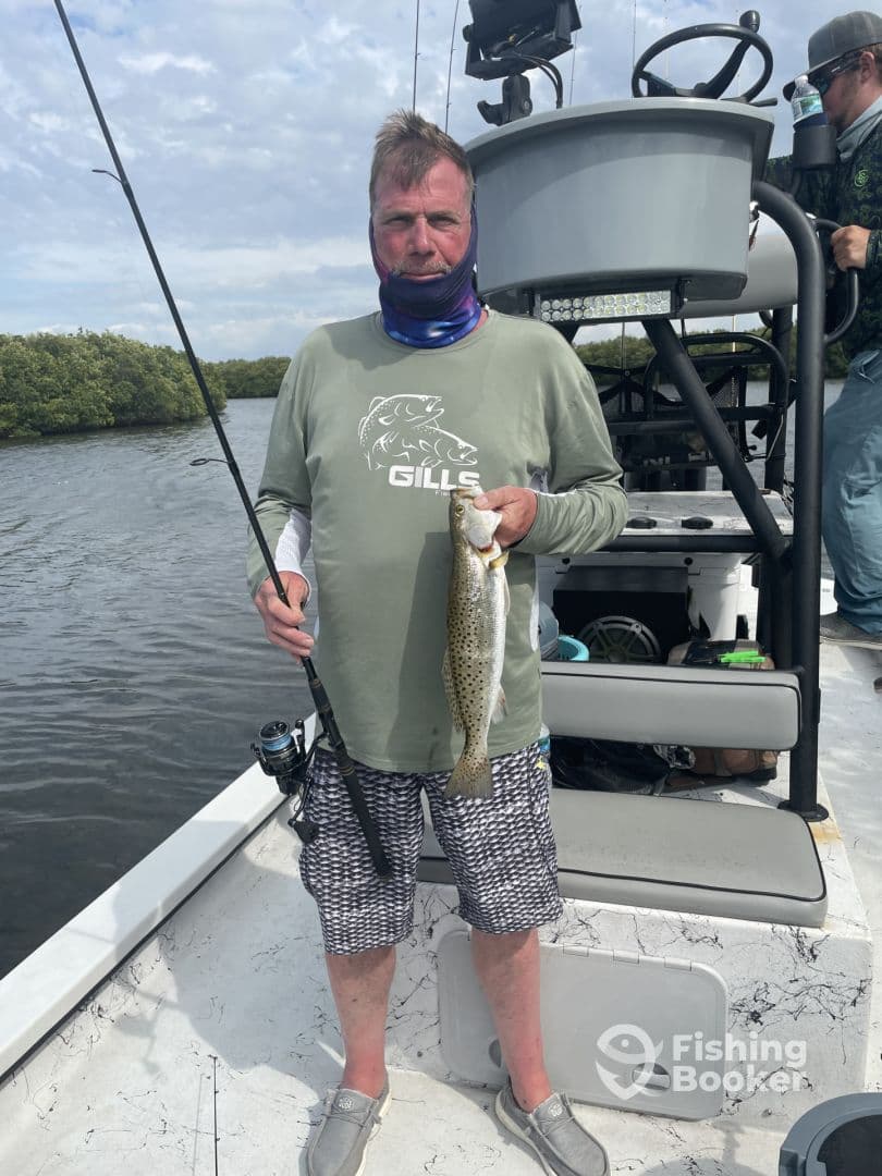 Angler holding a Speckled Trout while fishing from a boat in a coastal waterway, showcasing a successful catch during the trip.