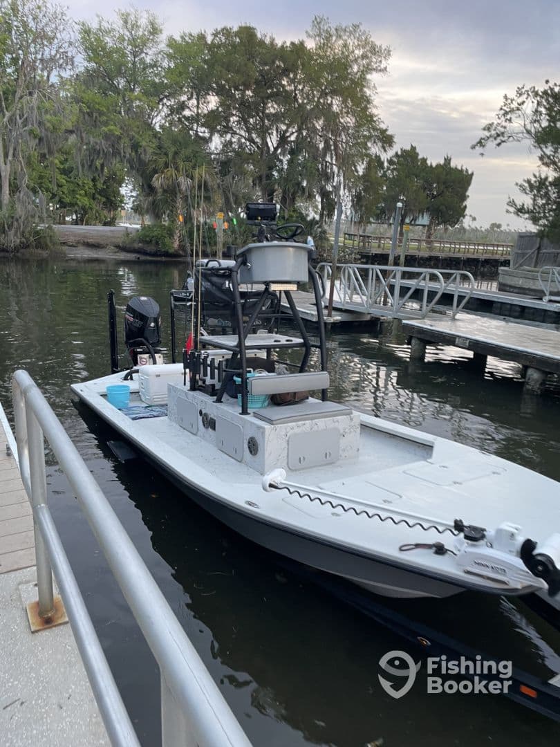 A sleek fishing boat docked at a serene waterfront, surrounded by lush greenery, ideal for a day of fishing.